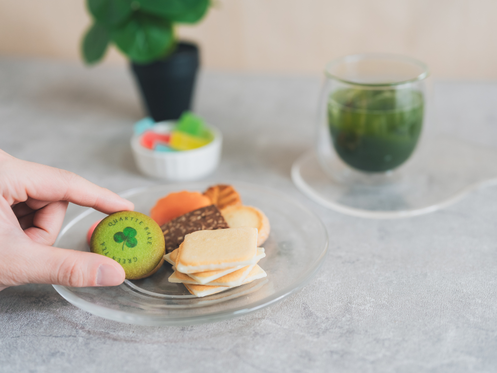 A Karutte Bake biscuit lifted lightly from the plate, with a chilled green tea resting quietly in the background.