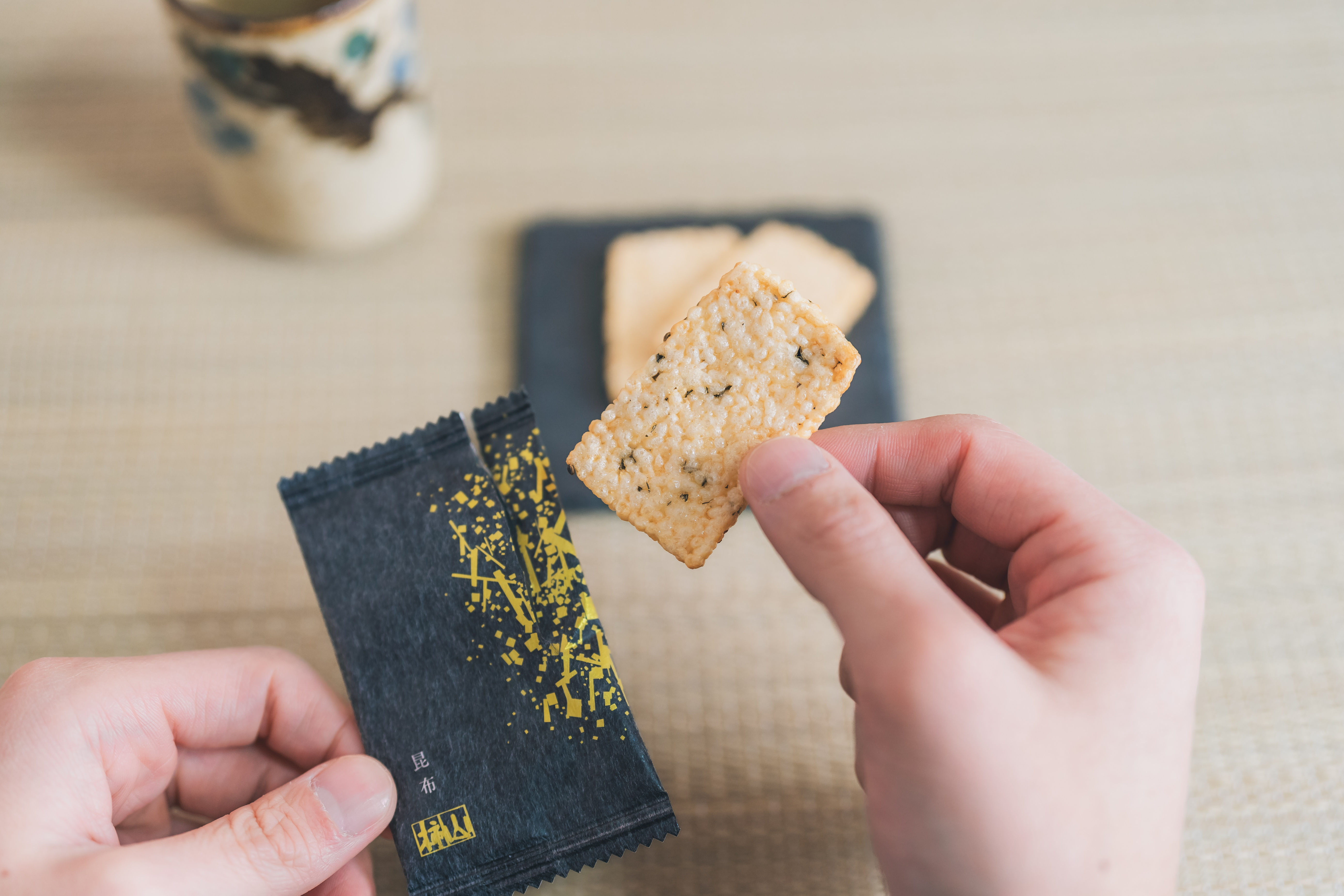 A single Keicho crisp taken from the packet, with a cup of Japanese tea waiting nearby.